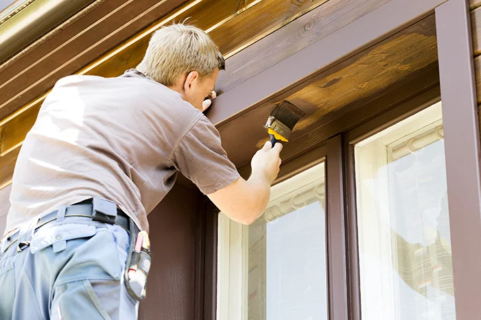 Person streicht Fensterrahmen mit Pinsel.